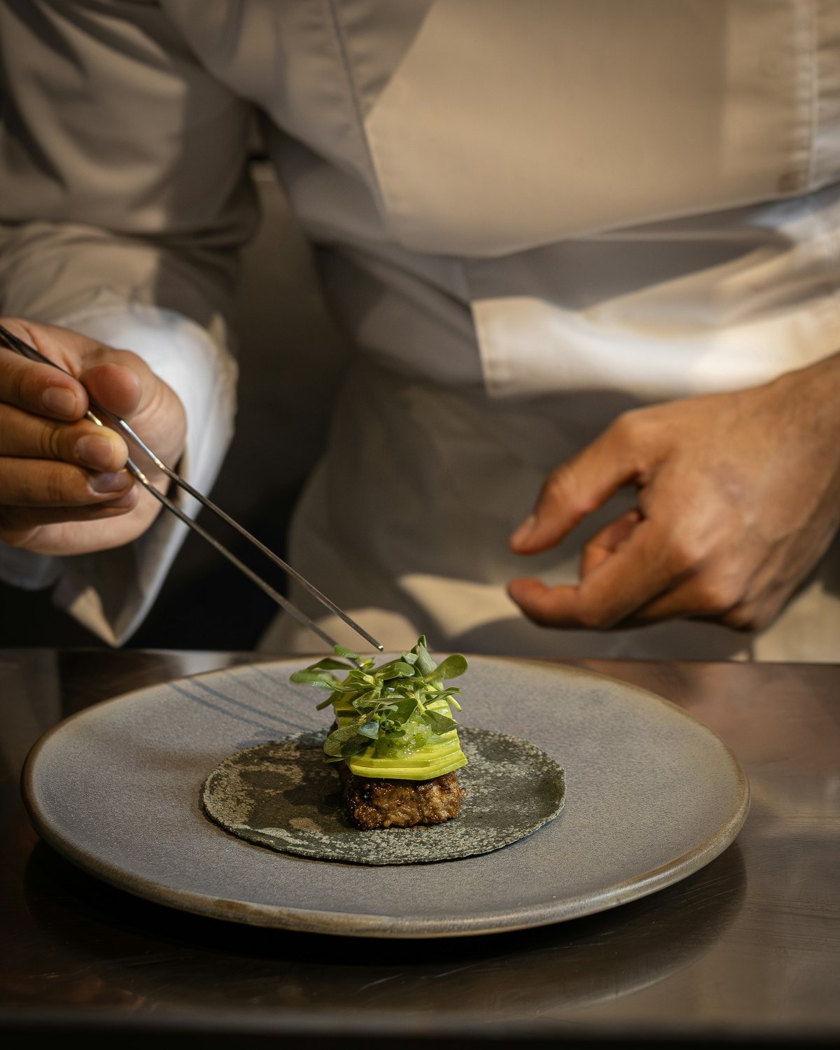 Un chef dresse une assiette à la pince