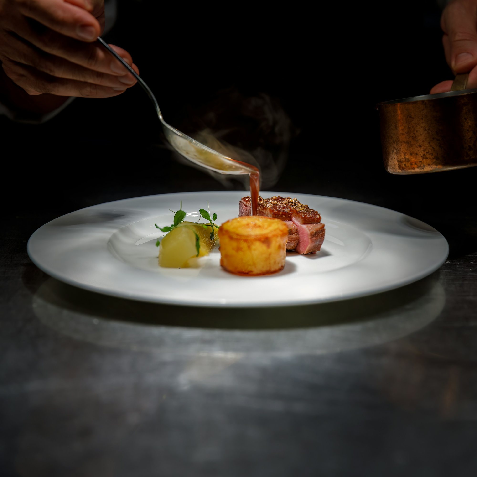 Un chef nappe une assiette de sa sauce, au passe